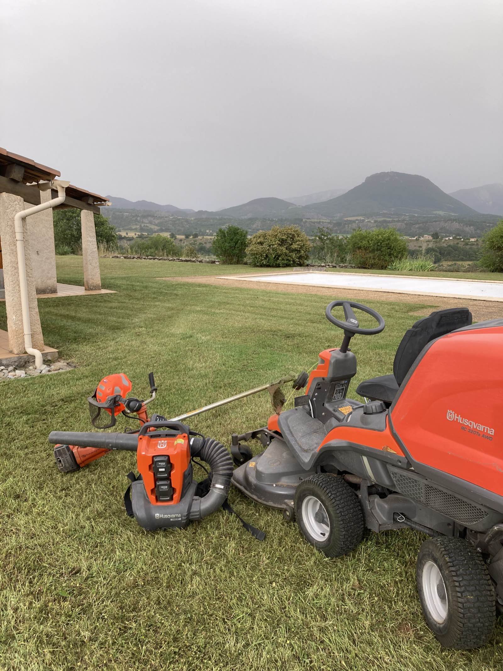 Tondeuse autoportée et matériel de jardinage sur une pelouse, avec les montagnes en arrière-plan